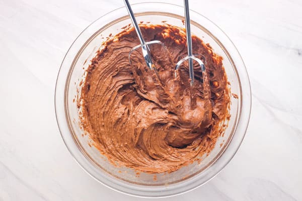 Glass bowl with a thick chocolate batter and beaters from a hand mixer.