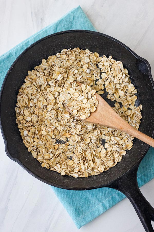 Overhead view of spoons stirring oats in a skillet.