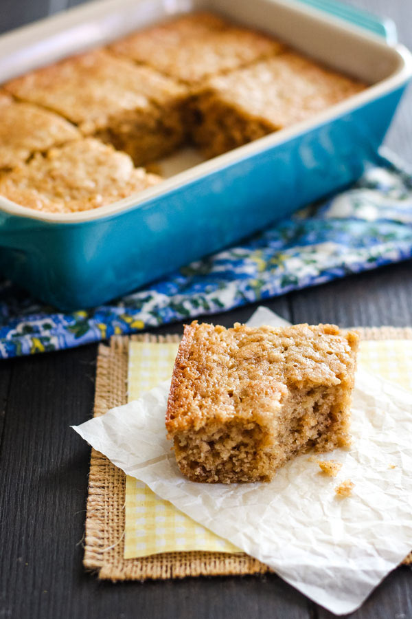 A piece of banana bread on parchment next to a small blue baking dish.