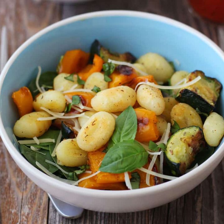 Closeup of roasted vegetables and gnocchi in a bowl on a wooden table.