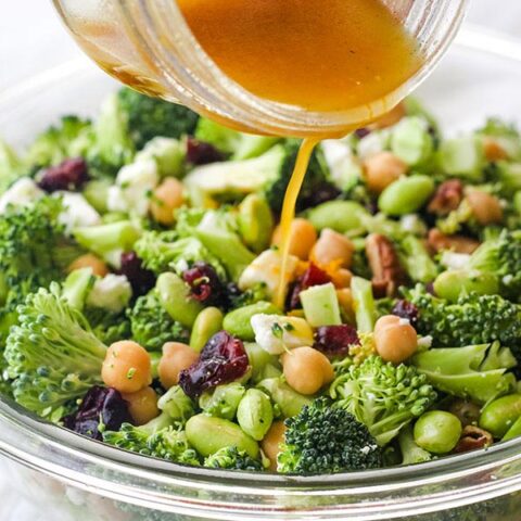 Hand pouring dressing from a mason jar over a broccoli salad.