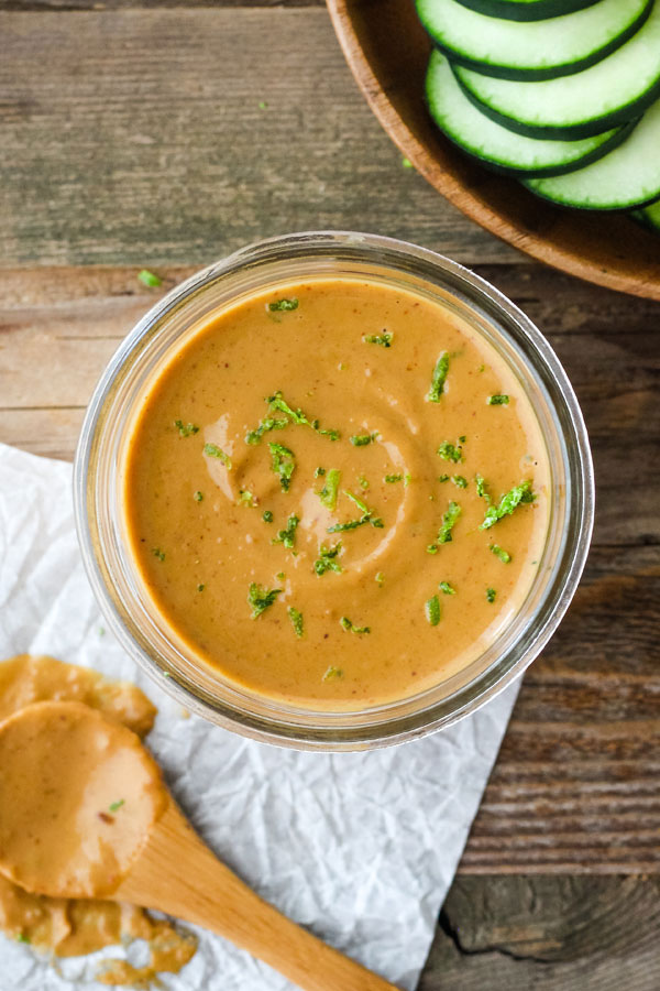 Peanut sauce in a glass mason jar with cucumber slices.