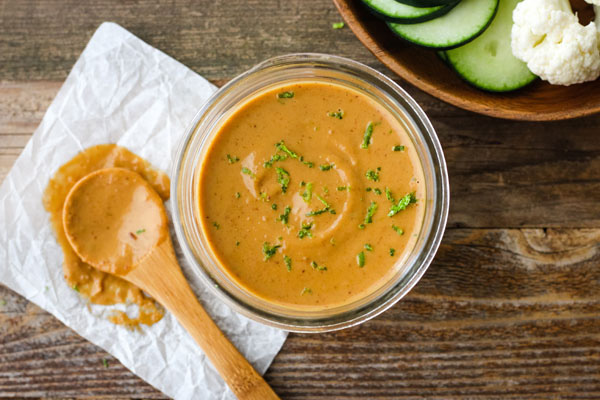 Peanut Lime Sauce in a glass mason jar next to a bowl of cucumber slices. 