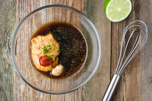 Peanut sauce ingredients in a glass bowl with a whisk.