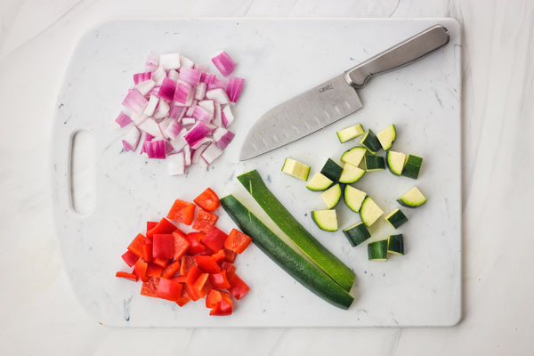 Chopped bell pepper, onion, and zucchini on a cutting board.