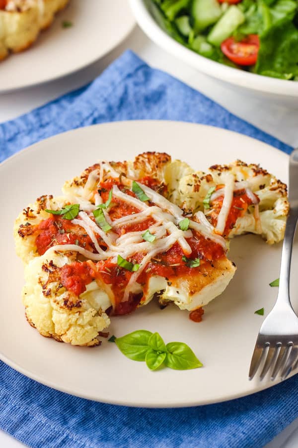 Pizza-style cauliflower steak on plate with fresh basil.