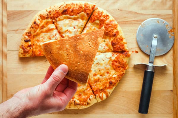 Hand holding slice of pizza with browned crust.