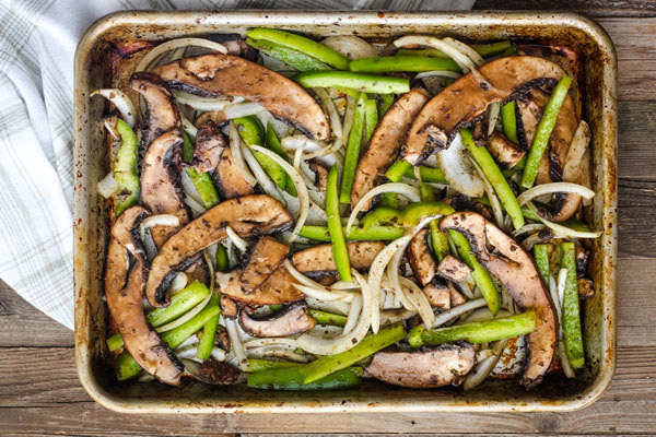 Marinaded mushrooms, peppers, and onions on a quarter sheet pan.