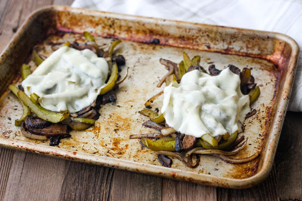 Two piles of roasted vegetables with cheese melted on a sheet pan.