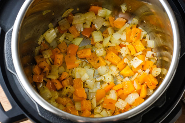 Diced onions and orange bell pepper inside an instant pot. 