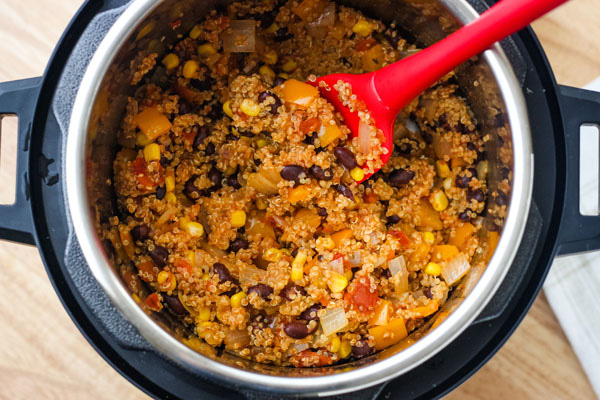 Cooked salsa quinoa in an instant pot with a red silicone spatula.