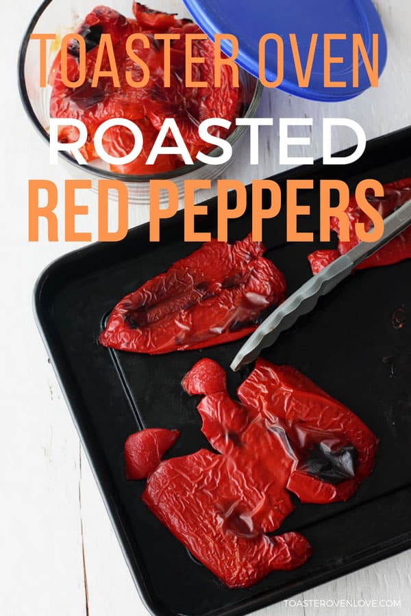 Cooked red peppers on a dark roasting pan with tongs.