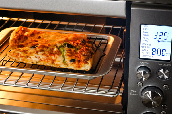 Pizza slices on a rack and pan inside of a toaster oven.