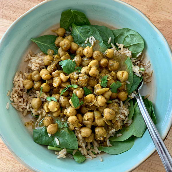 A blue bowl with brown rice, spinach, and chickpea curry.