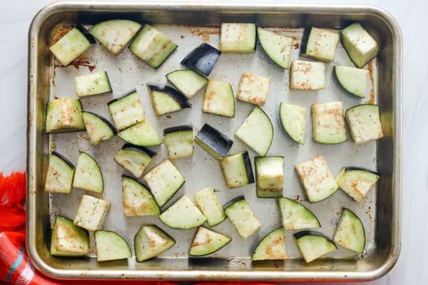 Overhead view of cut eggplant on rimmed sheet pan.