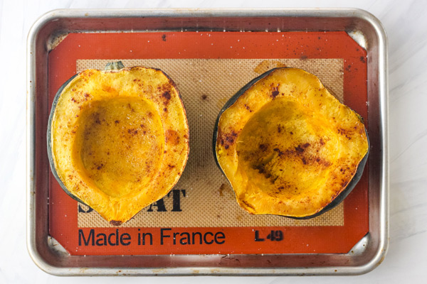 Overhead view of cinnamon roasted acorn squash halves on a baking sheet.