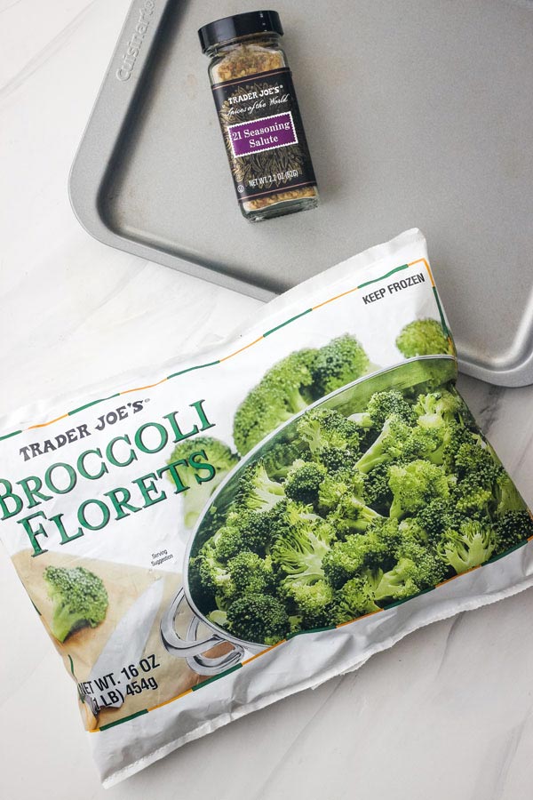 A bag of frozen broccoli florets, jar of seasoning, and metal sheet pan.