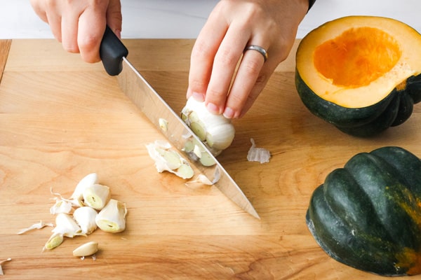 Hands slicing garlic on a cutting board.