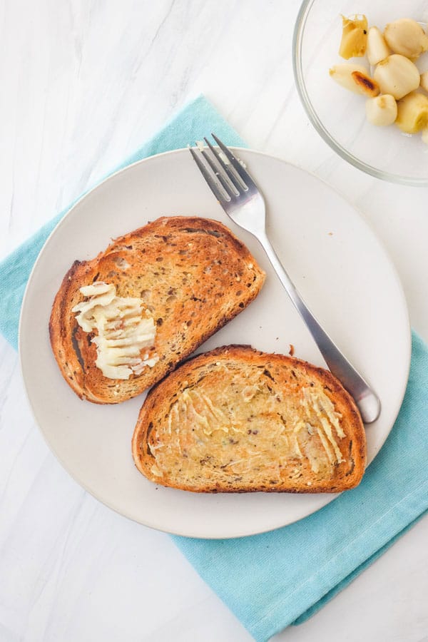 Plate of toasted bread spread with buttery roasted garlic.