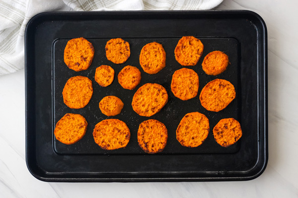 Cooked sweet potato rounds on a dark roasting pan.