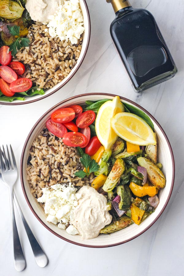 Veggie hummus bowls on a white table with forks and a bottle of balsamic.