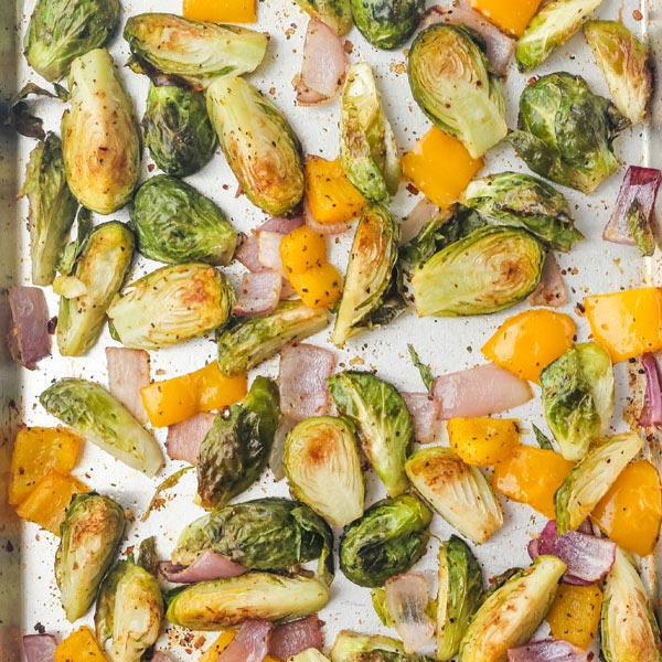 Roasted brussels sprouts, yellow bell pepper, and red onion on a sheet pan.