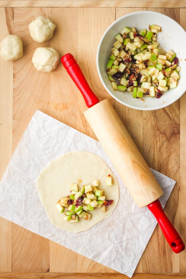 Rolled out dough topped with apple filling on a cutting board with a rolling pin.