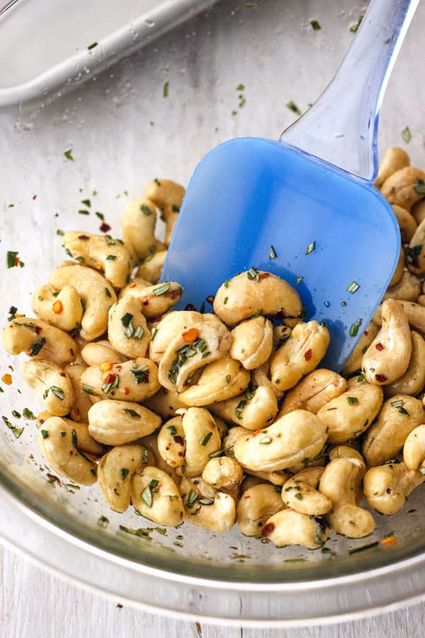 Seasoned nuts in a glass bowl with a rubber spatula.