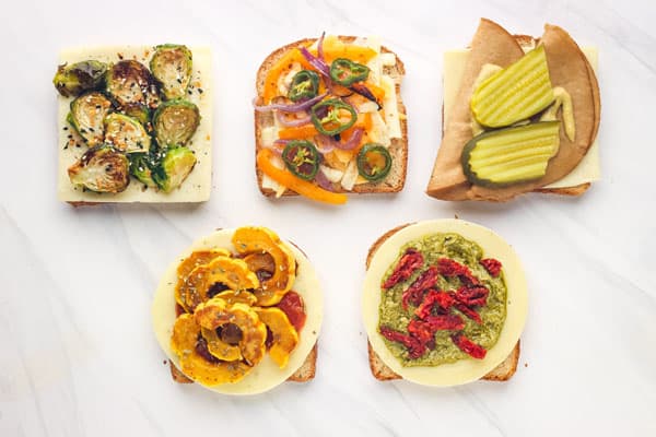 Overhead view of bread slices with a variety of cheeses and fillings.