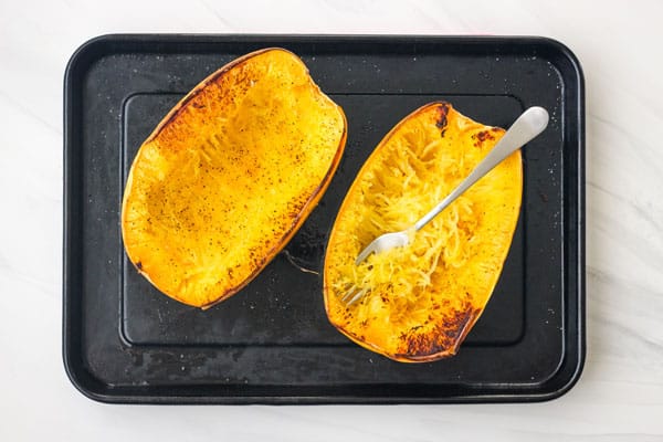 Fork scraping cooked spaghetti squash into strands.