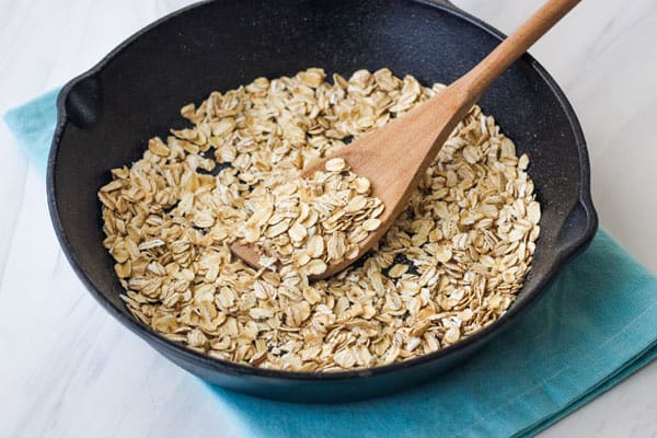 Cast iron skillet with spoon stirring toasted oats.