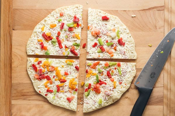 Wooden cutting board with a large frozen pizza sliced into four quarters.