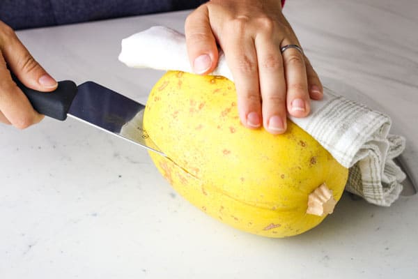 Person slicing into the side of a spaghetti squash.