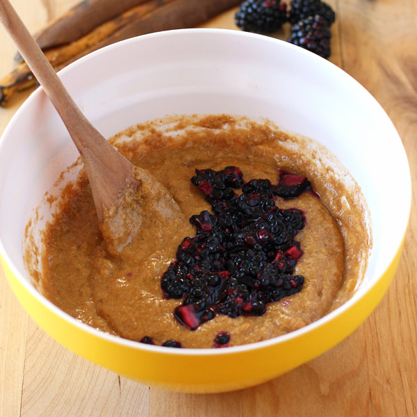 A yellow bowl with batter, chopped blackberries and a wooden spoon.