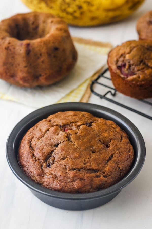 A white table with a small round pan of bread, muffins on a rack, and a mini bundt.