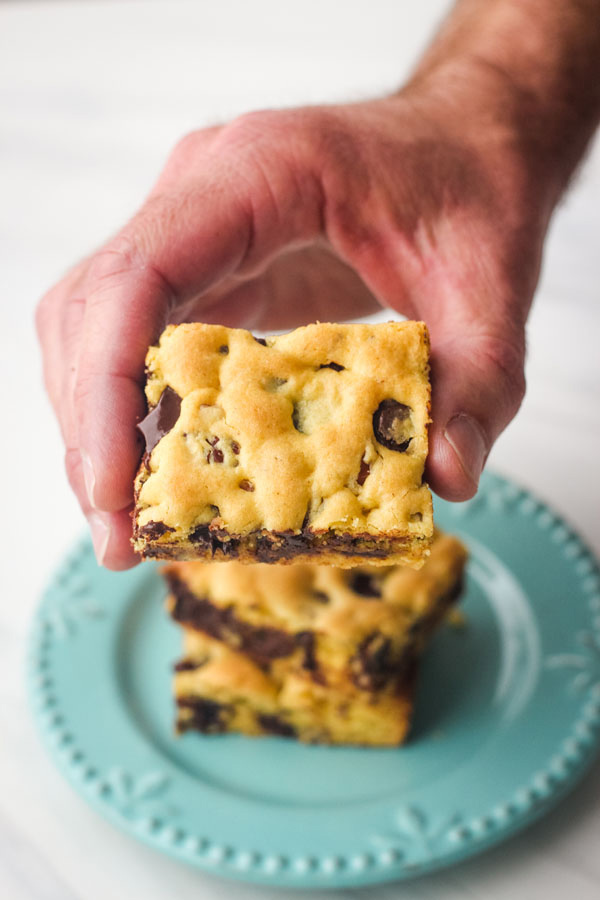 A hand holding a cookie bar in front of a blue plate. 