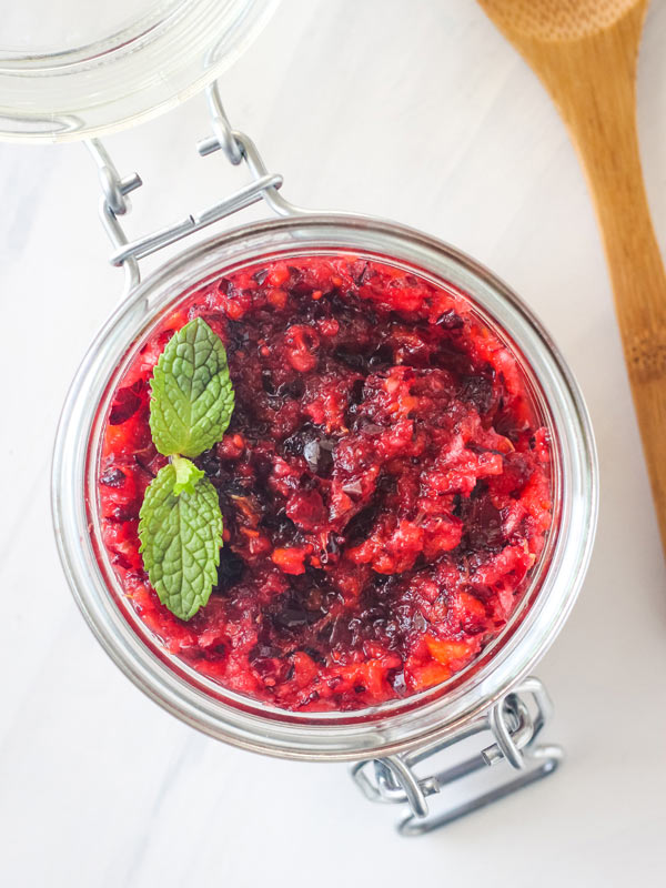 Cranberry relish in a glass mason jar with a sprig of fresh mint.