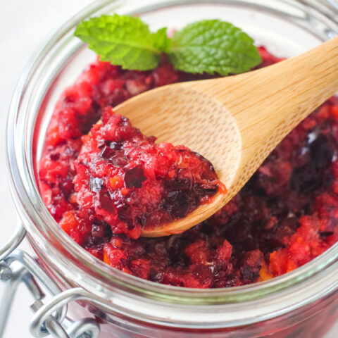 A small wooden spoon scooping relish out of a glass mason jar.
