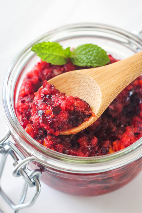 A small wooden spoon scooping relish out of a glass mason jar.