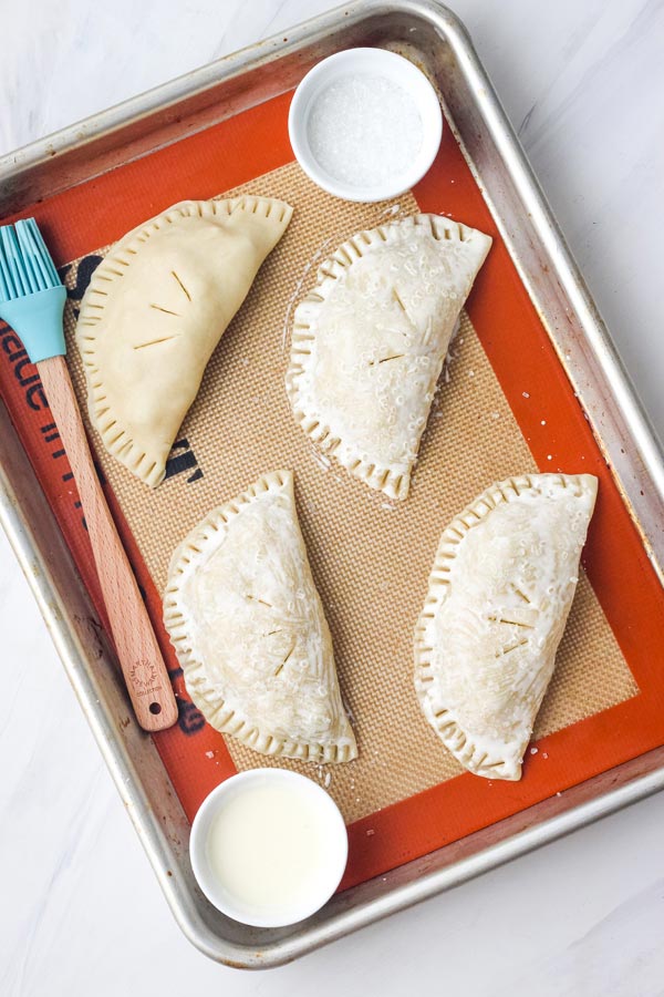 Hand pies brushed with cream on a quarter sheet pan lined with a silicone baking mat.