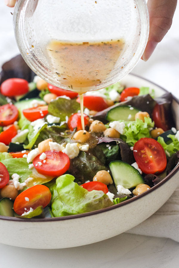 Hand pouring dressing from a mason jar onto a bowl of salad.