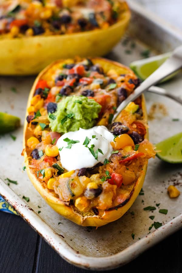 Spaghetti squash half with a fork sticking out of it on a metal baking sheet.