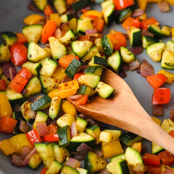 Skillet with cooked vegetables on a wooden spoon.