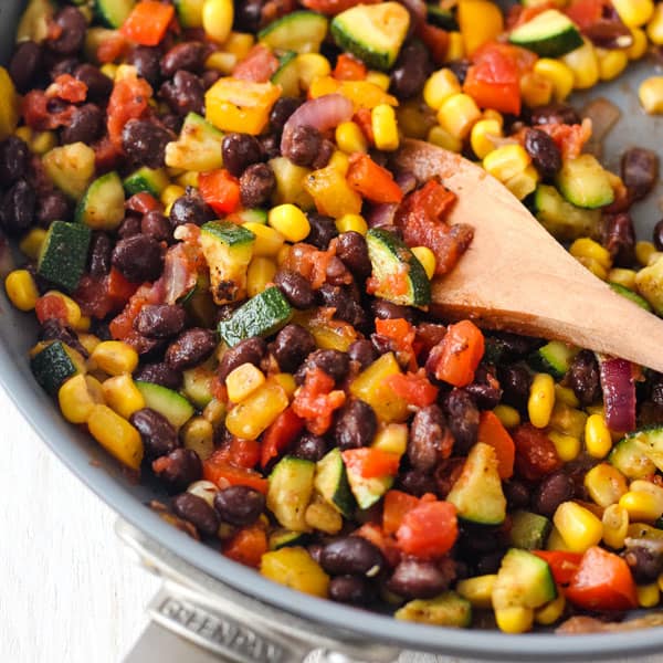 Skillet with cooked vegetables and salsa on a wooden spoon.