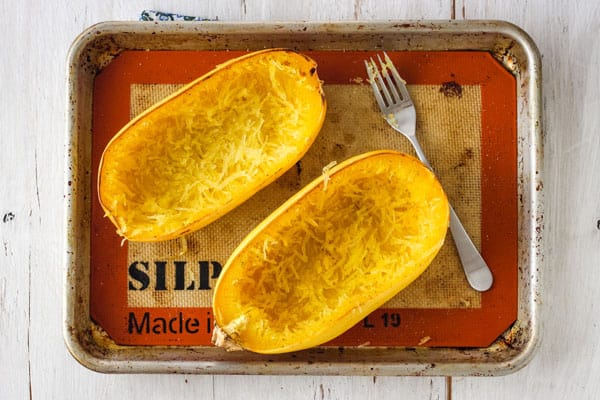 Scrapped spaghetti squash bowls on a silpat lined baking sheet with a fork.