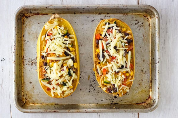 Overhead view of stuffed spaghetti squash halves topped with shredded cheese.