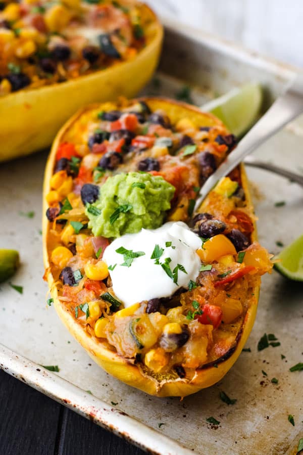 Cooked spaghetti squash bowl topped with Greek yogurt and guacamole on a baking sheet.