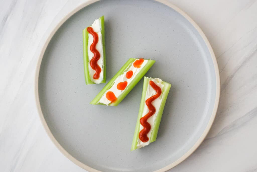 Celery pieces with cream cheese and squiggles of hot sauce.