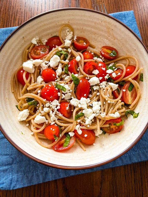 Overhead view of a bowl of pasta with grape tomatoes, feta, and basil.