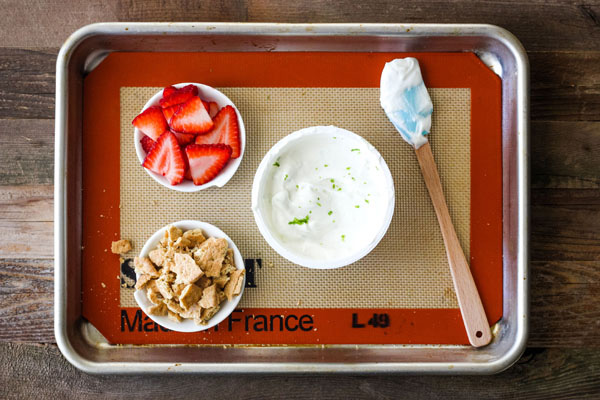 Yogurt, sliced strawberries and crumbled graham crackers on a baking sheet.